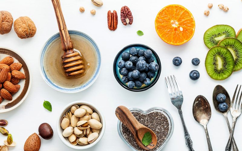 Ingredients for a healthy foods background nuts honey berries fruits blueberry orange almonds walnuts and chia seeds .The concept of healthy food set up on white wooden background. Flat lay.