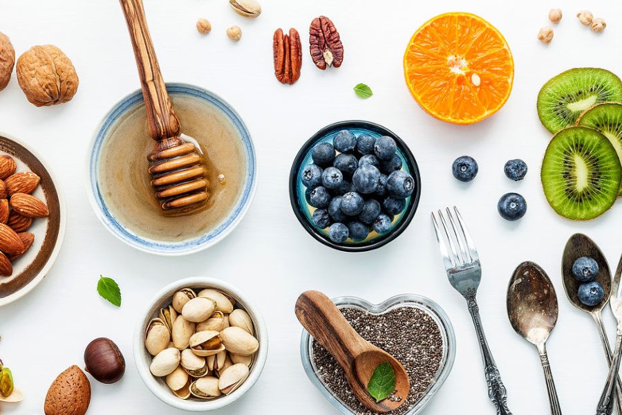 Ingredients for a healthy foods background nuts honey berries fruits blueberry orange almonds walnuts and chia seeds .The concept of healthy food set up on white wooden background. Flat lay.